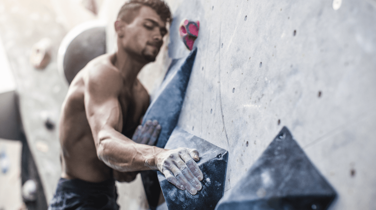 man using strength to hold onto climbing wall