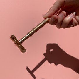 mio gold safety razor in front of pink background