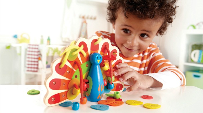 Product testers wanted: A young boy playing with a Hape Lacing Peacock toy.