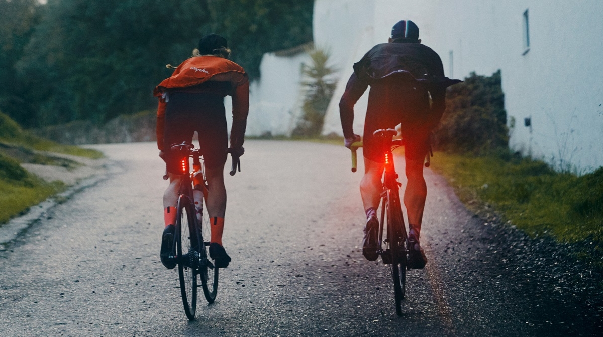 two cyclists riding their bikes in winter with lights on