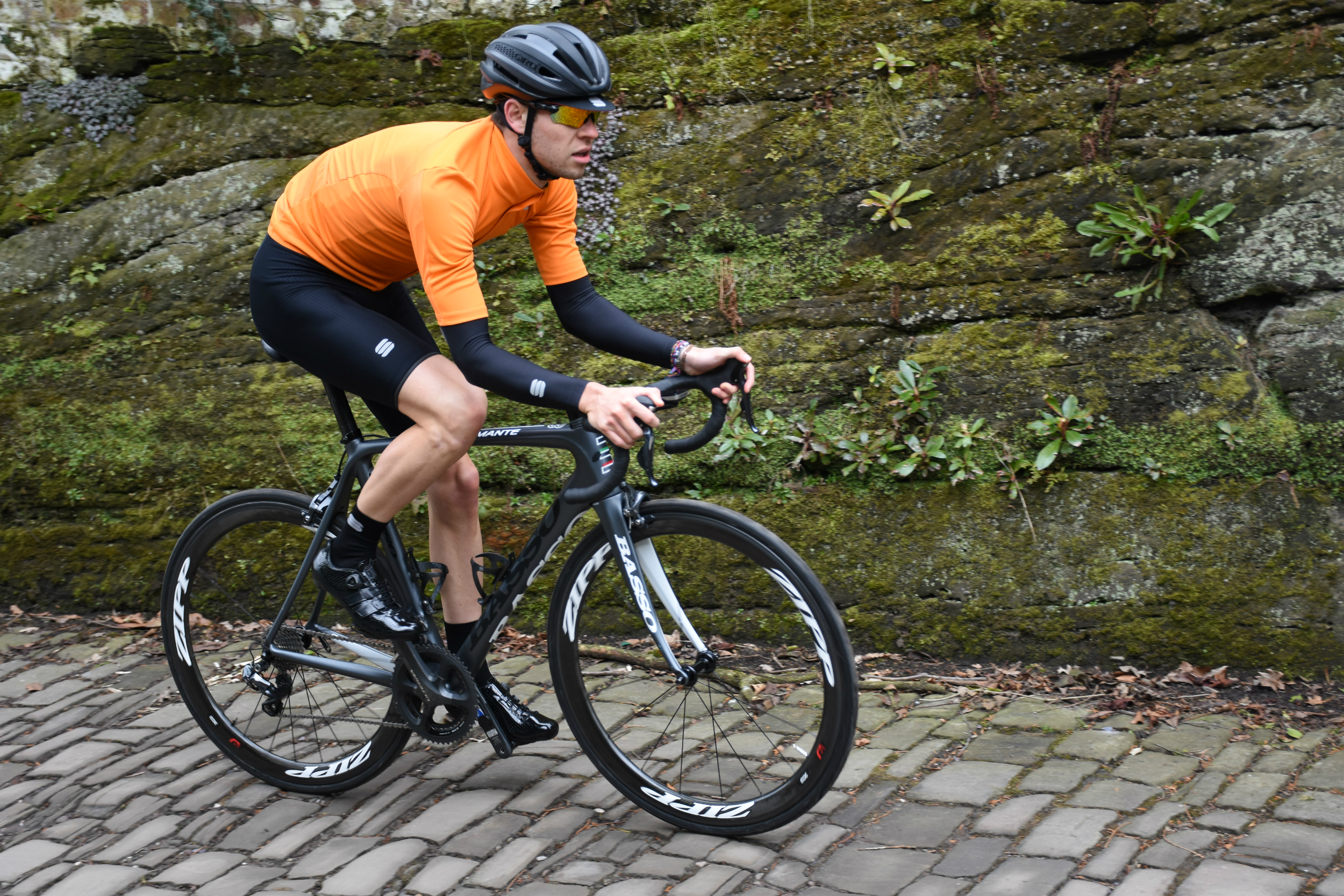 a cyclist riding on cobbles in the fiandre light jersey in bright orange