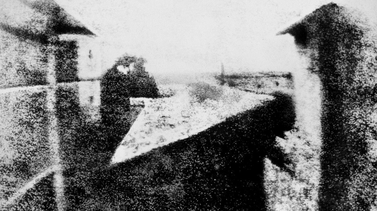 black and white image of a view from a window onto buildings and the surrounding countryside