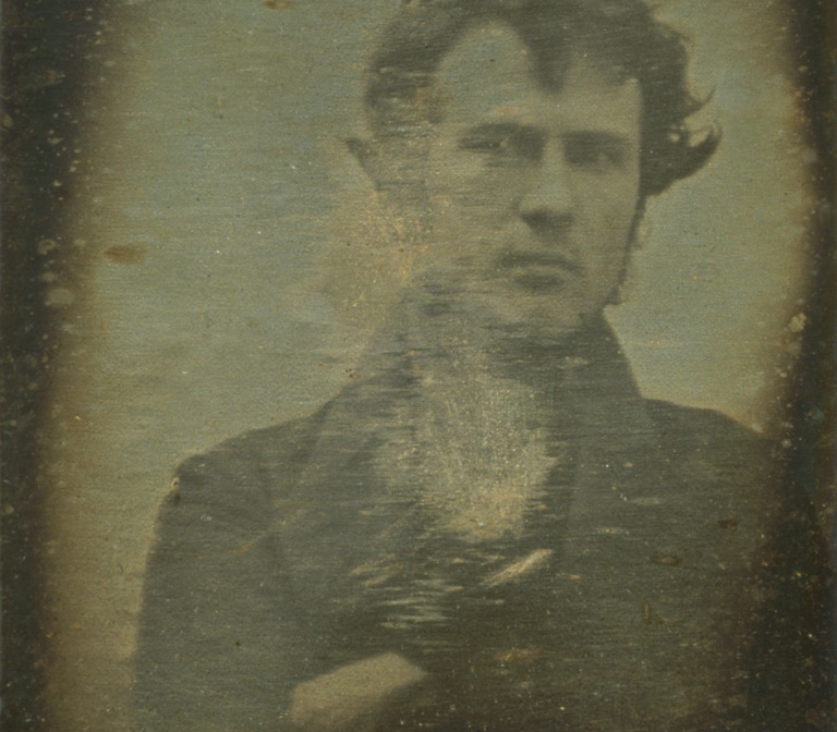 a sepia self-portrait of Robert Cornelius folding his arms