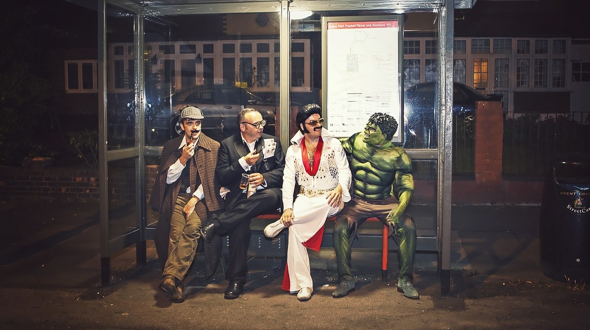 a man dressed in full sherlock holmes garb alongside other popular figures on a bus stop bench in a residential area at night