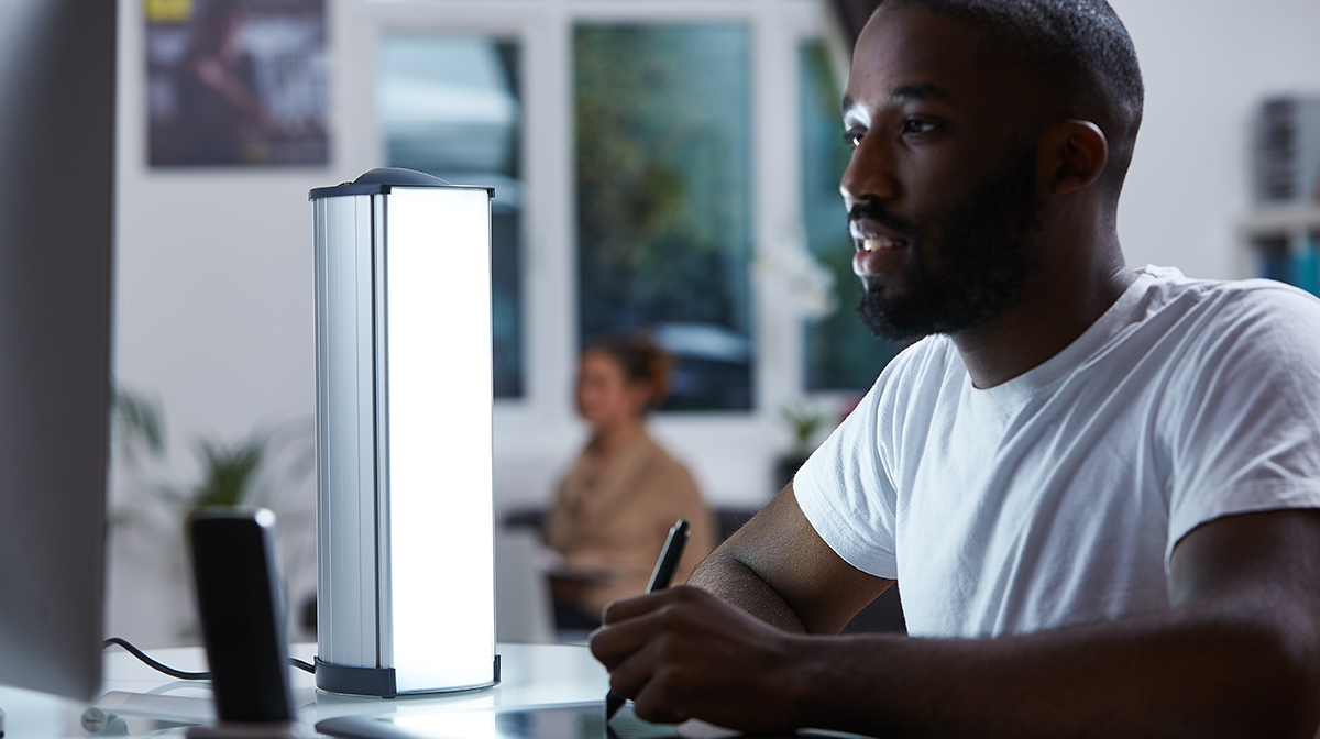 Lumie lamp on table with man writing