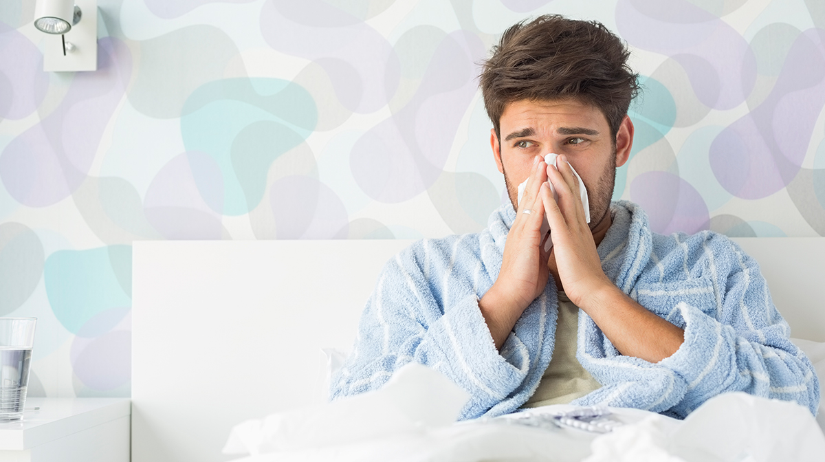 Sick man blowing nose in bed