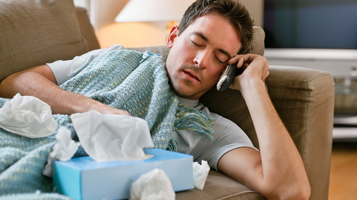 Man with flu holding tissues calling in sick.