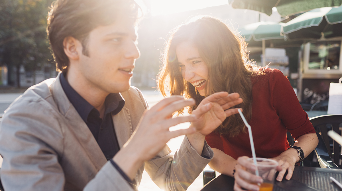 Woman laughing at boyfriend at a table outdoors