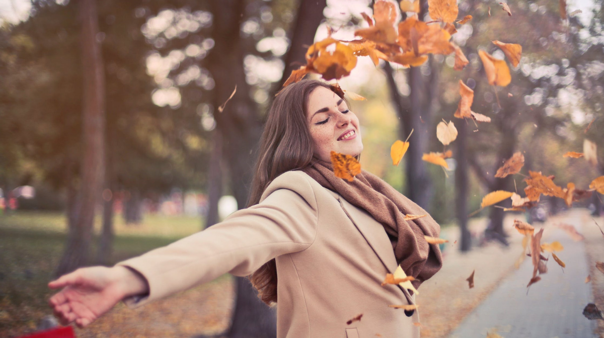woman in scarf staying healthy this autumn outside throwing up leaves