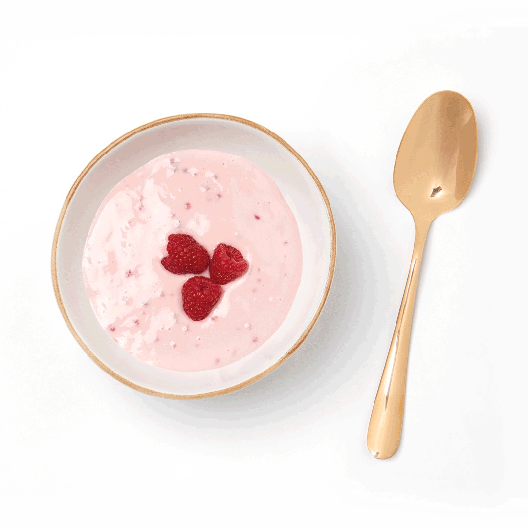 Spring yogurt in bowl topped with raspberries and gold spoon
