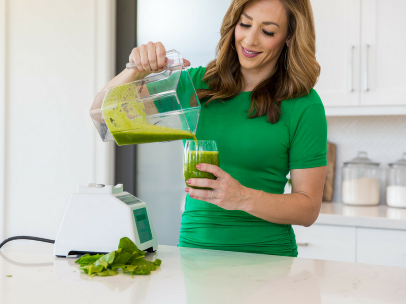 A woman pouring a green detox drink from a blender into a glass