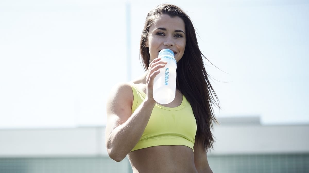 Frau trinkt aus Wasserflasche auf Sportplatz