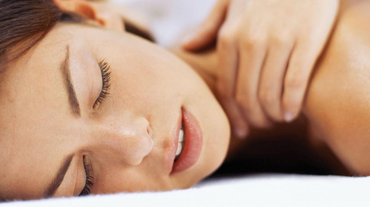 A woman lying on a bed enjoying a neck massage spa treatment
