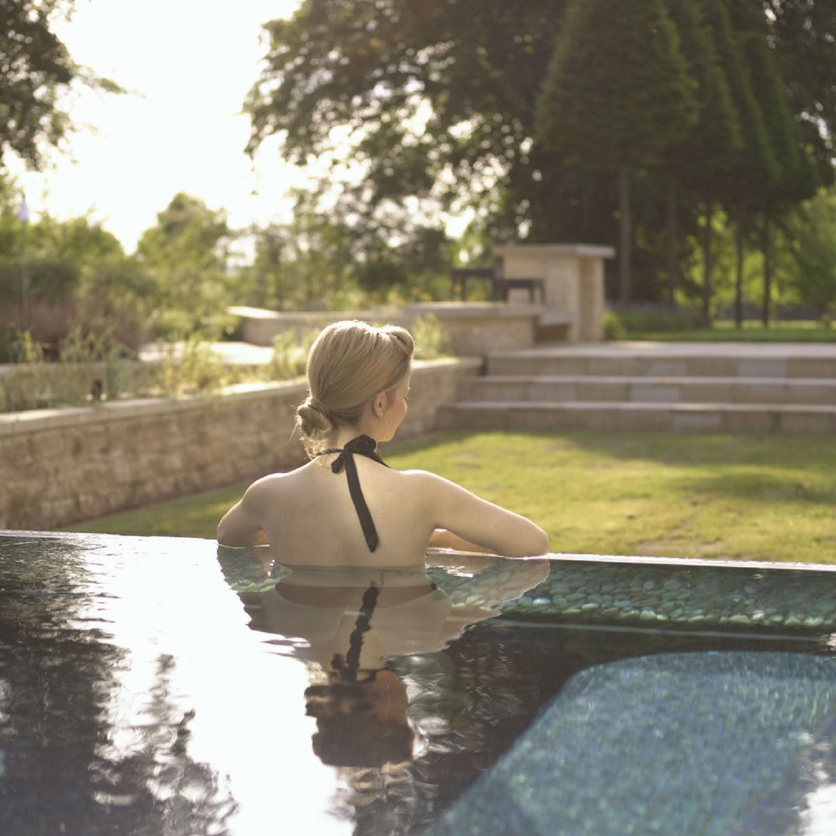 Lady in an outdoor pool overlooking the gardens of Lucknam Park on a sunny day