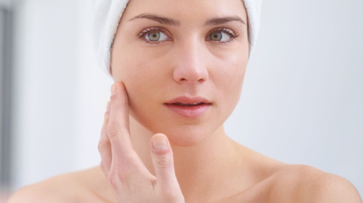 Woman in a towel touching her face in a mirror, flawless natural skin