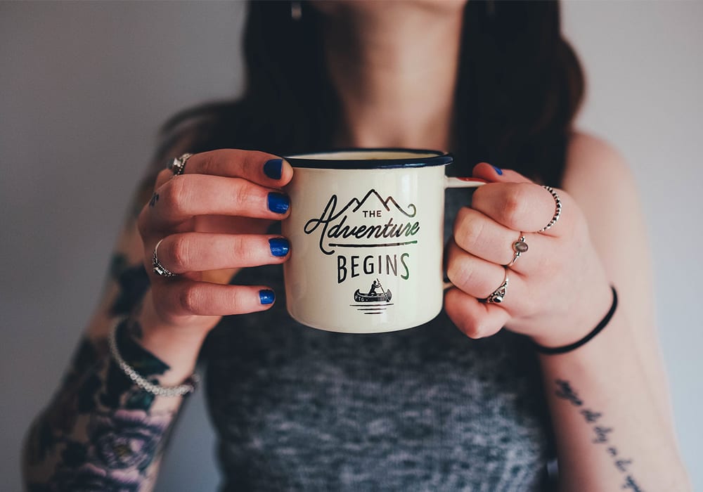 Tattowierte Frau hält Kaffebecher hoch, The Adventure begins, girl with coffeecup tattoo