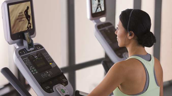 woman watching tv while exercising on gym equipment