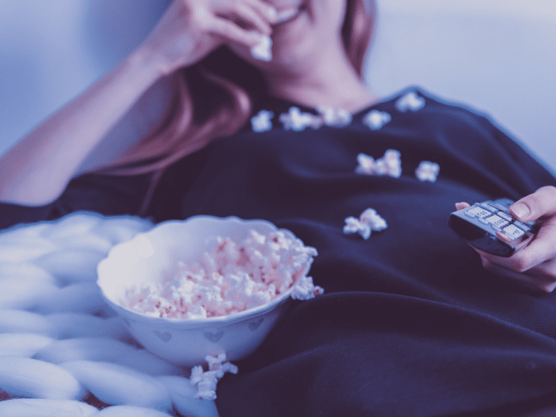 a woman eating a bowl of popcorn while watching a movie on the couch