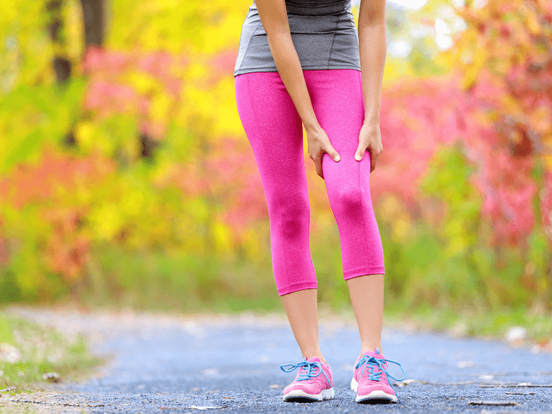A woman holding her leg during a jog because of sore leg muscles