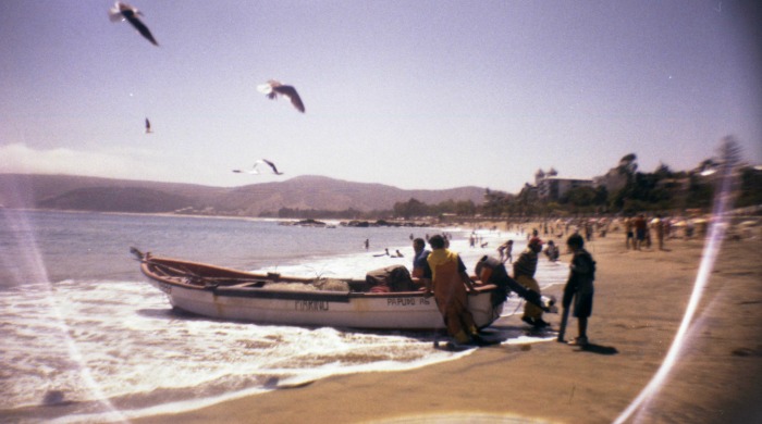 Lomography La Sardina: a boat on a beach being pushed into the sea.