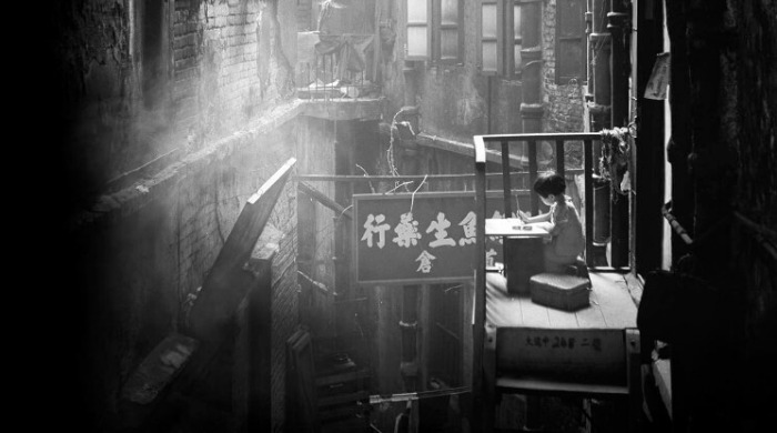 The Streets of 1950s Hong Kong Fan Ho: a young boy on a balcony overlooking a crowded back alley.