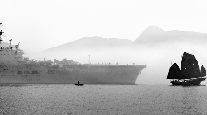 The Streets of 1950s Hong Kong Fan Ho: A traditional boat dwarfed next to a large, modern ship with mountains behind in the mist.