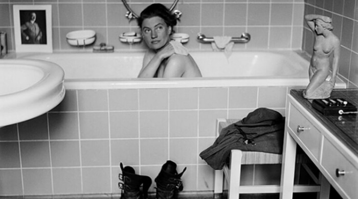 Lee Miller A Woman's War: A woman in a bath with soldier's boots and coat on the floor in front.