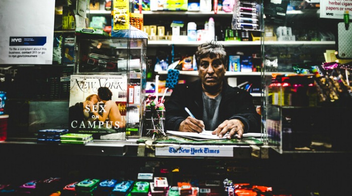 The Streets of New York City by Shaquel Munroe: A shopkeeper at his kiosk in an off-licence.