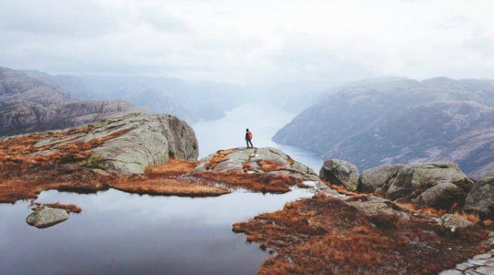 Alex Strohl Fjords of Norway: A man standing in at the edge of a cliff looking into the fjords and lakes beyond.