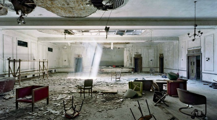 Ruins of Detroit Yves Marchand Romain Meffre: A spacious, once grand room with rubble and overturned chairs littering the floor.