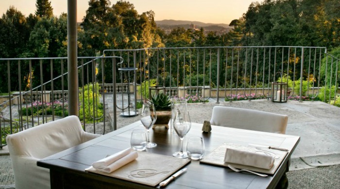Il Salviatino, Florence: A table for two set on a balcony overlooking the landscape and surrounding trees.
