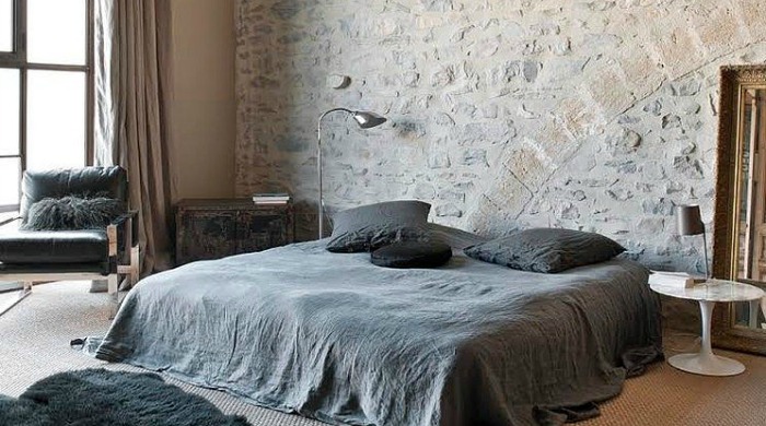 A bedroom in this renovated mill with dark grey bed linen on a low double bed against an old stone wall.