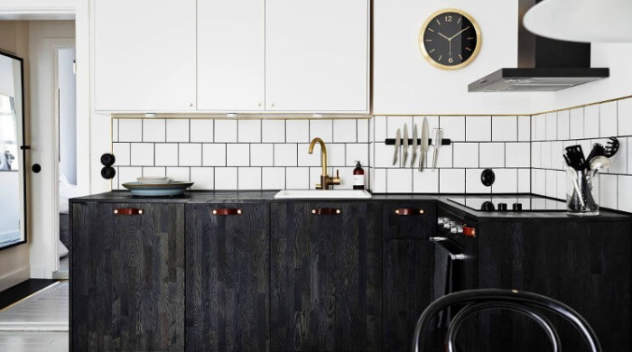 A black and white kitchen with a gold clock and bronze tap to show how to use metallics and copper in the home.