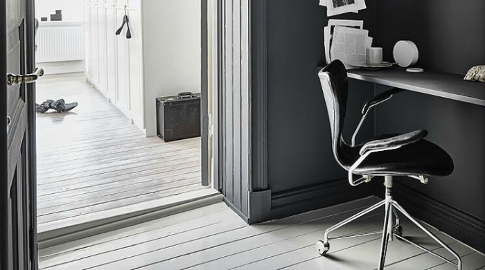 An office incorporating the dark wall interior trend with charcoal grey walls and door contrasted with a white hallway.