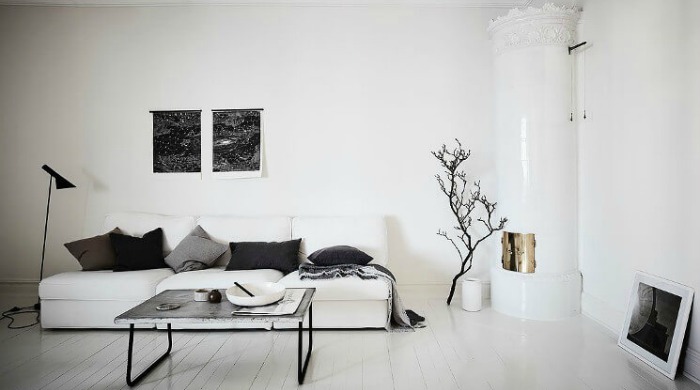 A white living room incorporating black metal accents with a black standing lamp and a concrete table with black metal legs.