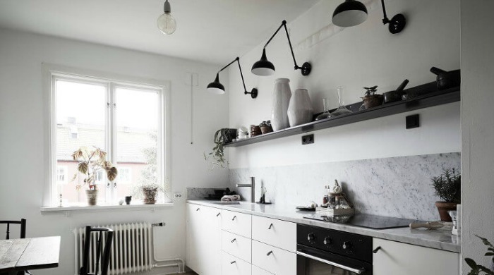 A white kitchen incorporating black metal accents with black lamps fixed above the kitchen shelves.