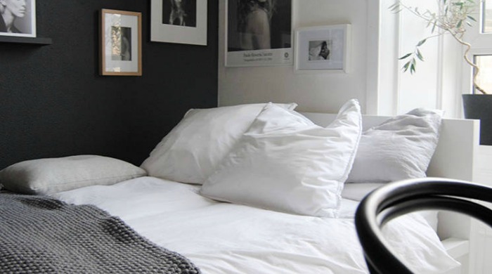 A monochrome bedroom with black and white walls, a white bed and white painted floorboards, and black and white phortographs on the walls.