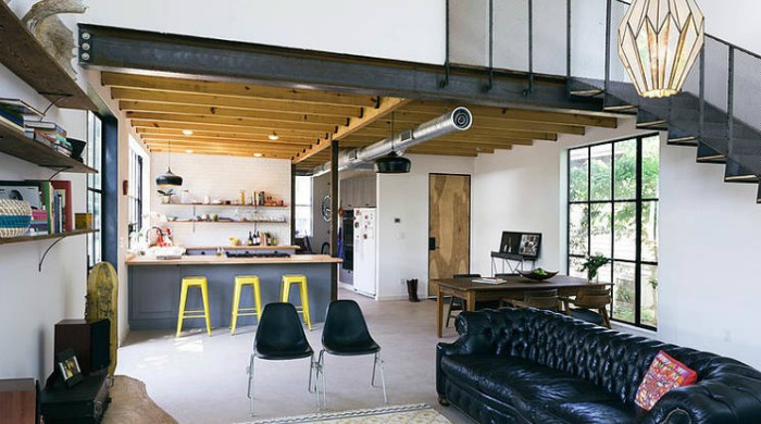 A monochrome living area with white walls and flooring, black chairs, and exposed brown wooden beams.