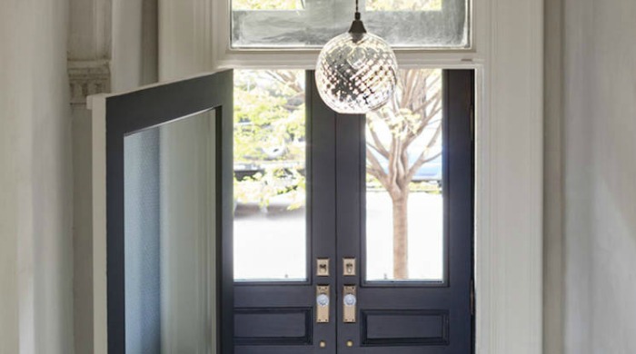 A set of navy blue double doors with a spherical glass light fitting above them leading into the hallway of the New York brownstone.