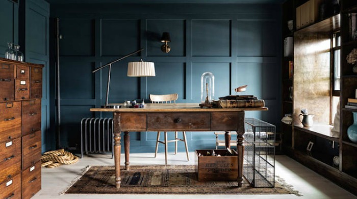 The study in a New York brownstone with navy blue paneled walls and dark brown wooden furniture, including a desk, sets of drawers and lamps.