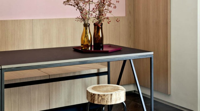 Vases of dried flowers on a black table with a log stool, with light brown wooden panels on pastel pink coloured walls in a modern Turin home.