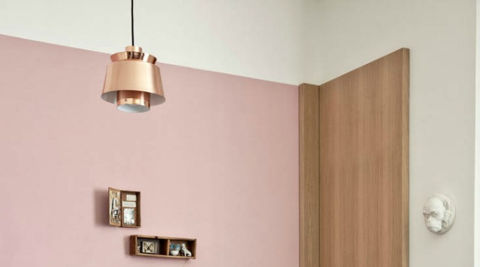 A copper hanging light against a white and pastel pink wall with a wooden panel in a modern Turin home.