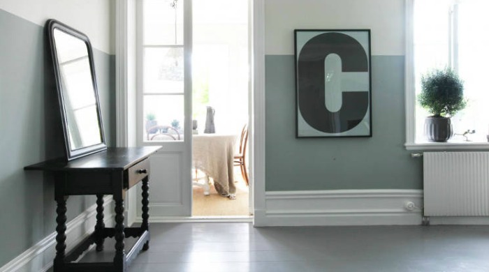 A room in a Swedish country house with pale green and white walls, a dark brown dressing table and mirror and a poster with the letter 'C' on it in a black frame.
