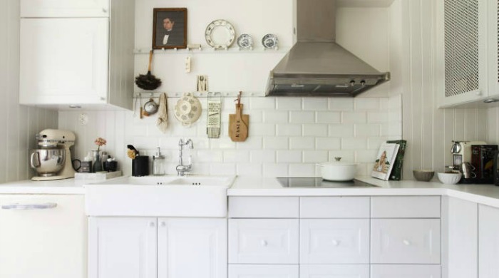 A white kitchen in a Swedish country house with a modern hob and extractor fan and traditional decor including china plates and a portrait painting.