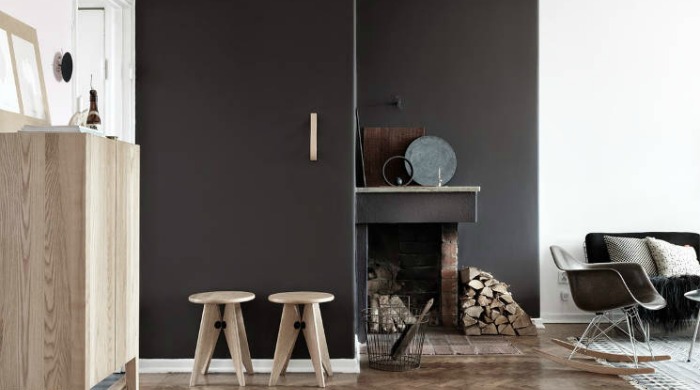 A room demonstrating the grey trend with a section of wall painted dark grey, with rustic decor including wooden chairs and a brick and metal fireplace.