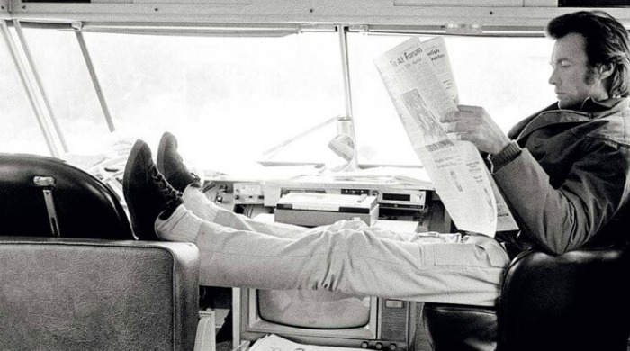 The Art of Behind the Scenes: Clint Eastwood sitting with his feet up in a mobile home reading a newspaper on the set of 'Joe Kidd'.