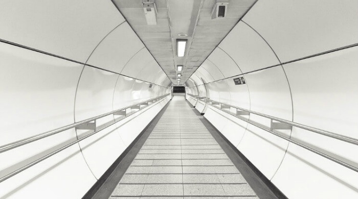 An empty pedestrian tunnel lit up brightly by white lighting in the London Underground series by Mark Cornick.