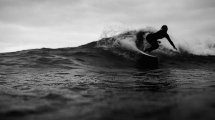 A black and white shot of a surfer riding a wave in the Ocean Culture series by Luke Paige.