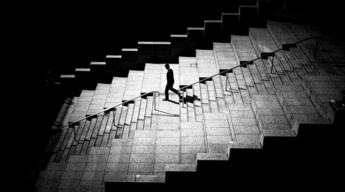 A man walking down a wide stariway in a spotlight surrounded by darkness by Junichi Hakoyama.