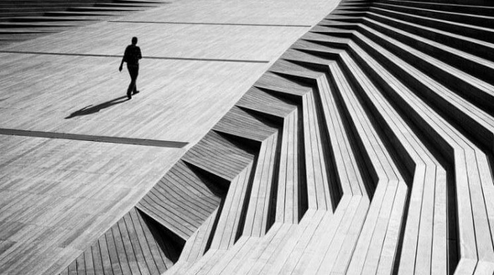 A person's silhouette walking across wooden-effect flooring with architectural lines to the right by Junichi Hakoyama.